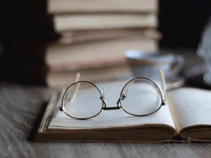 Stack of books, cup of tea, and reading glasses on an open book.
