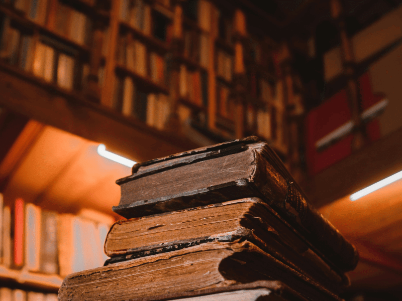 A stack of books against a background of bookshelves.